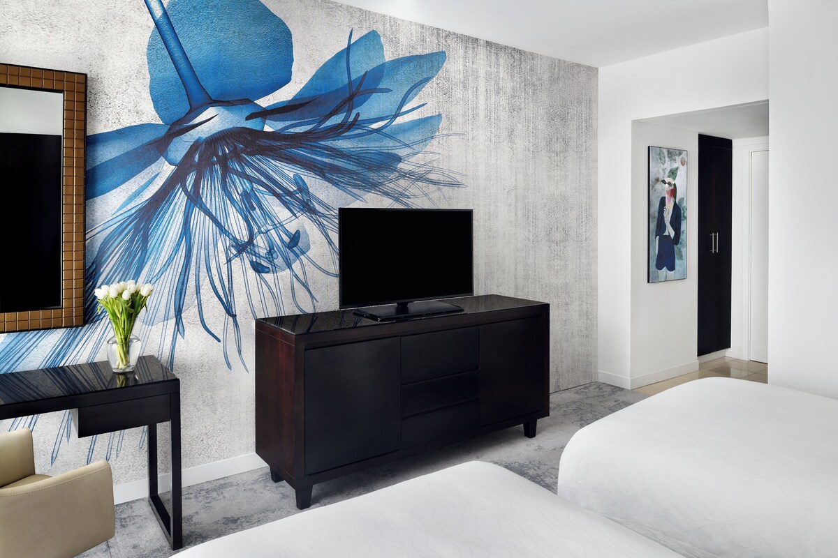 Habitación de hotel moderna con un gran mural floral, un televisor de pantalla plana, un aparador de madera oscura y una cama.