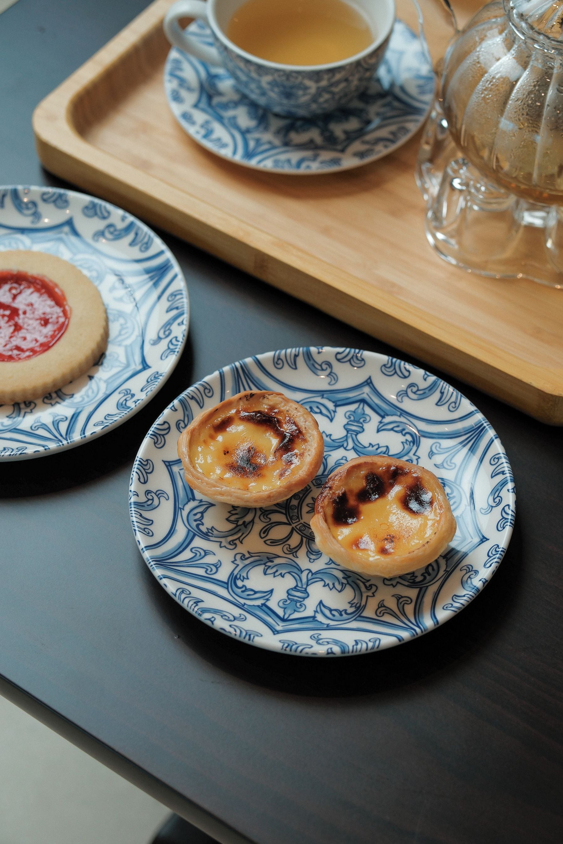 A table with two plates of Portuguese custard tarts, a cup of tea, and a glass of water on a tray.
