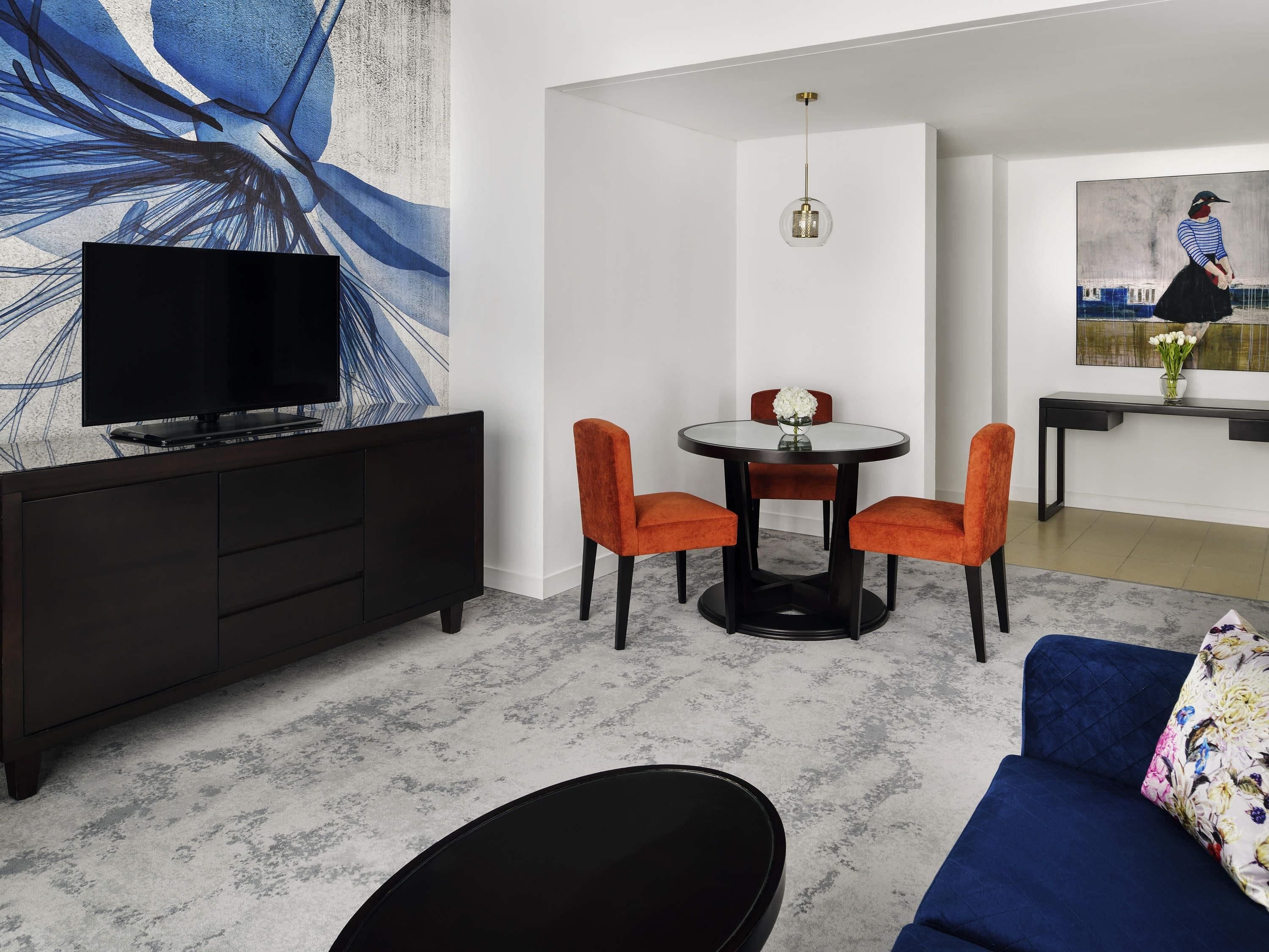 Uma sala de estar moderna com um sofá, uma mesa de jantar com cadeiras, uma TV em um móvel e obras de arte nas paredes.