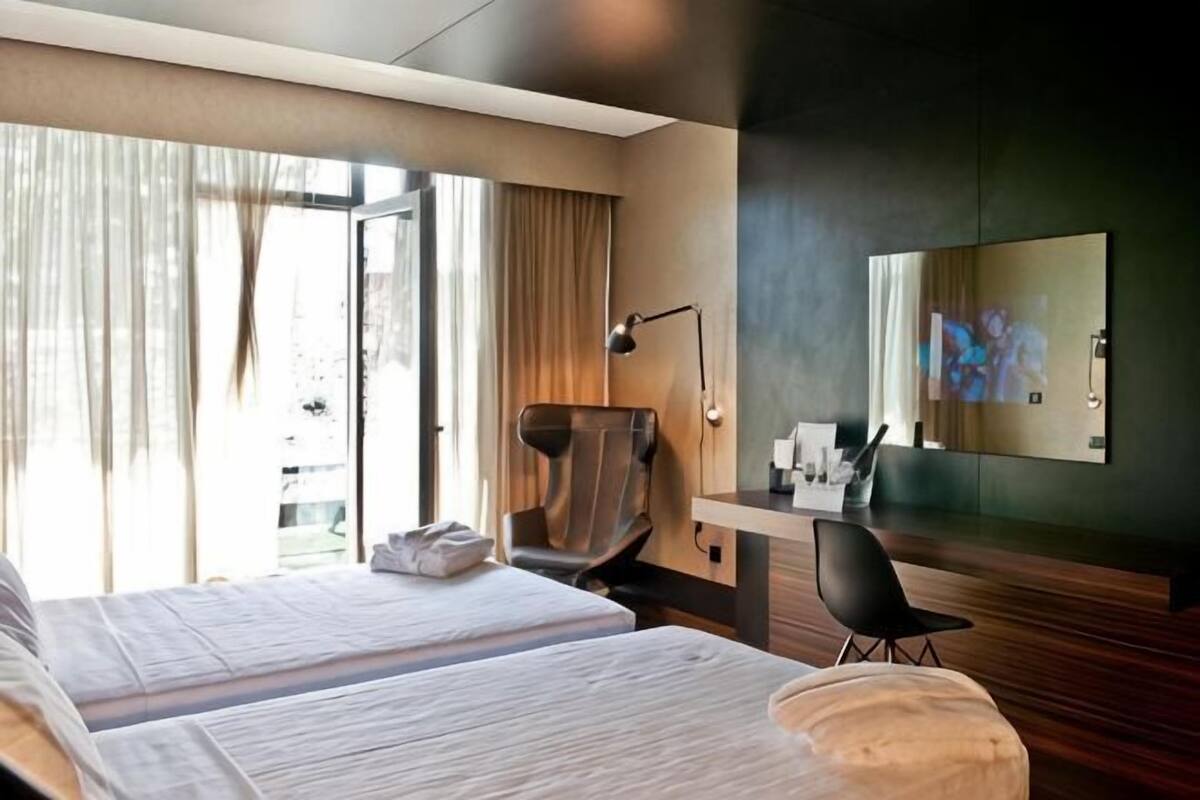 Een hotelkamer met twee bedden, een bureau, een stoel, een televisie en een groot raam met gordijnen.