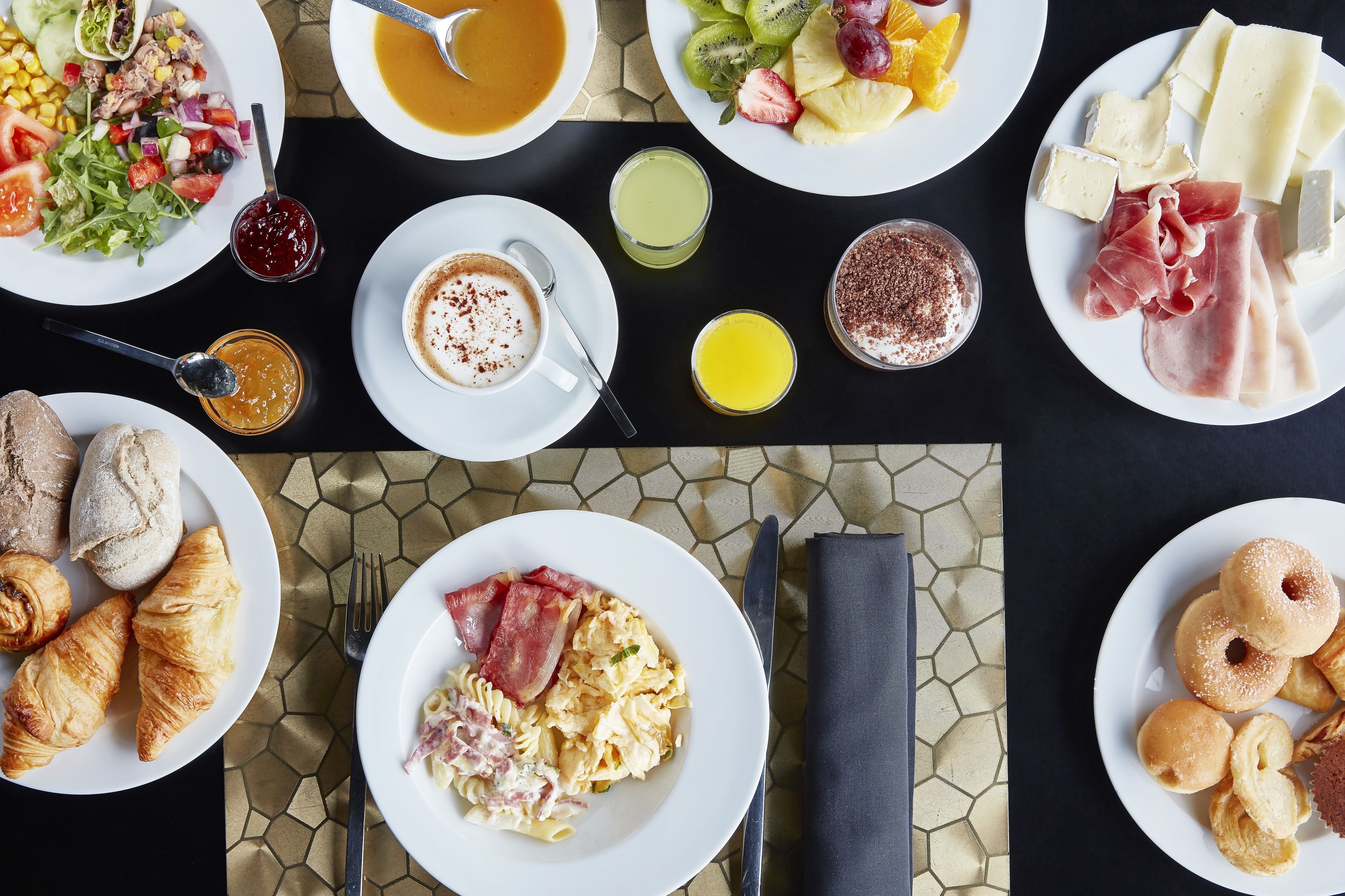 A breakfast buffet with various dishes, including eggs, pastries, and fruit.