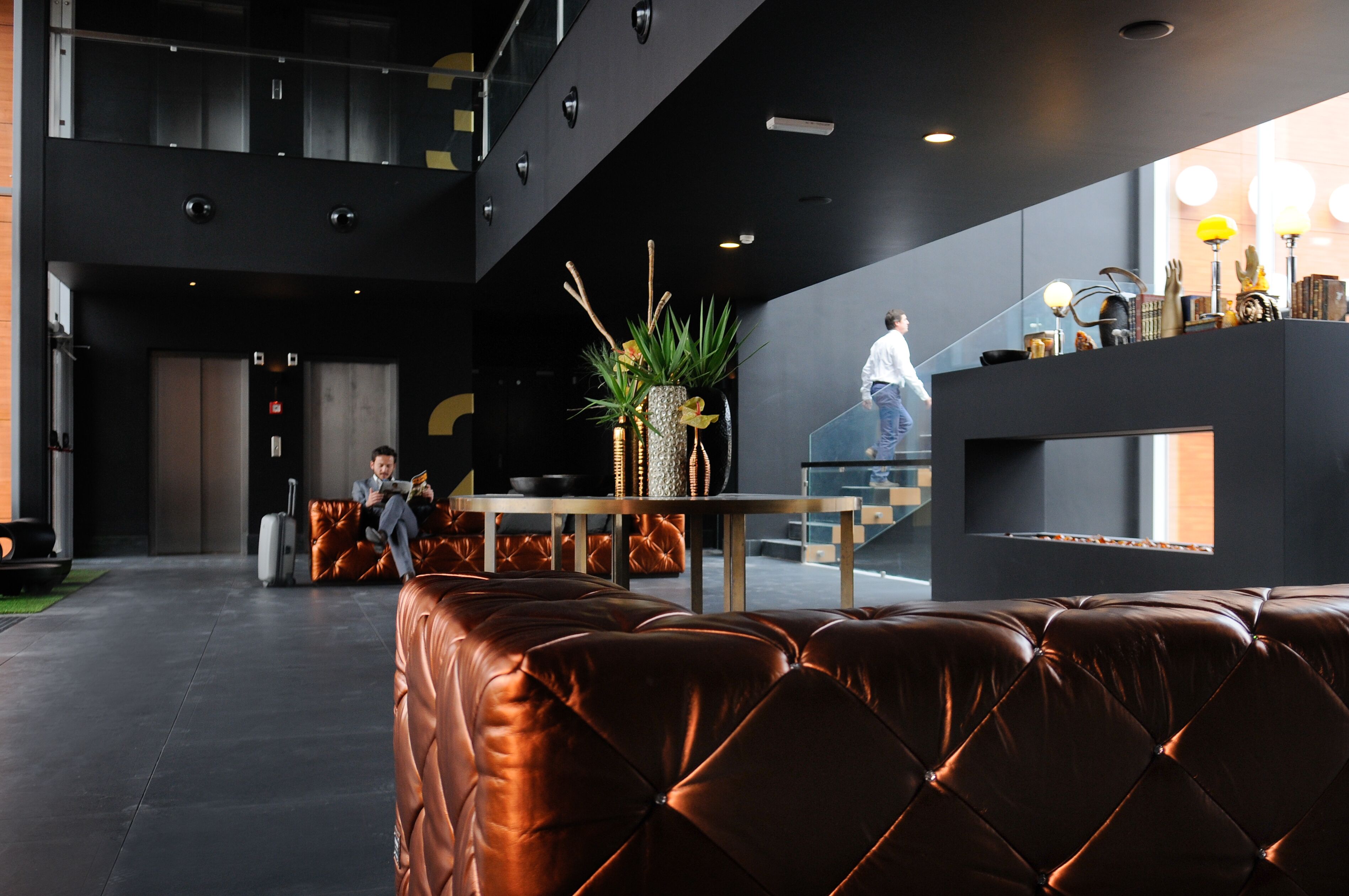 A modern lobby with leather seating, a staircase, and a reception area with decorative items.