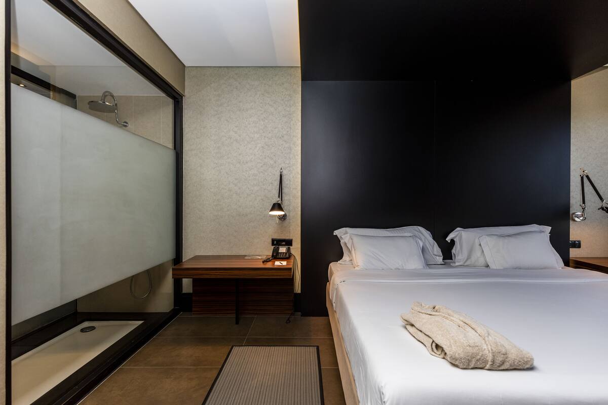 Een moderne hotelkamer met een groot bed, een bureau met telefoon, een bedlamp en een douchecabine van glas.