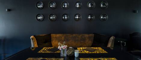 A modern dining area with a black table set for two, a vase with flowers, and a wall with circular mirrors.
