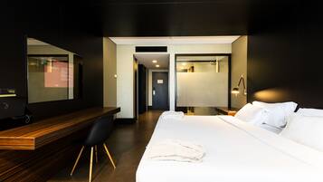 A hotel room with a wooden desk, a bed with white linens, and a large mirror.