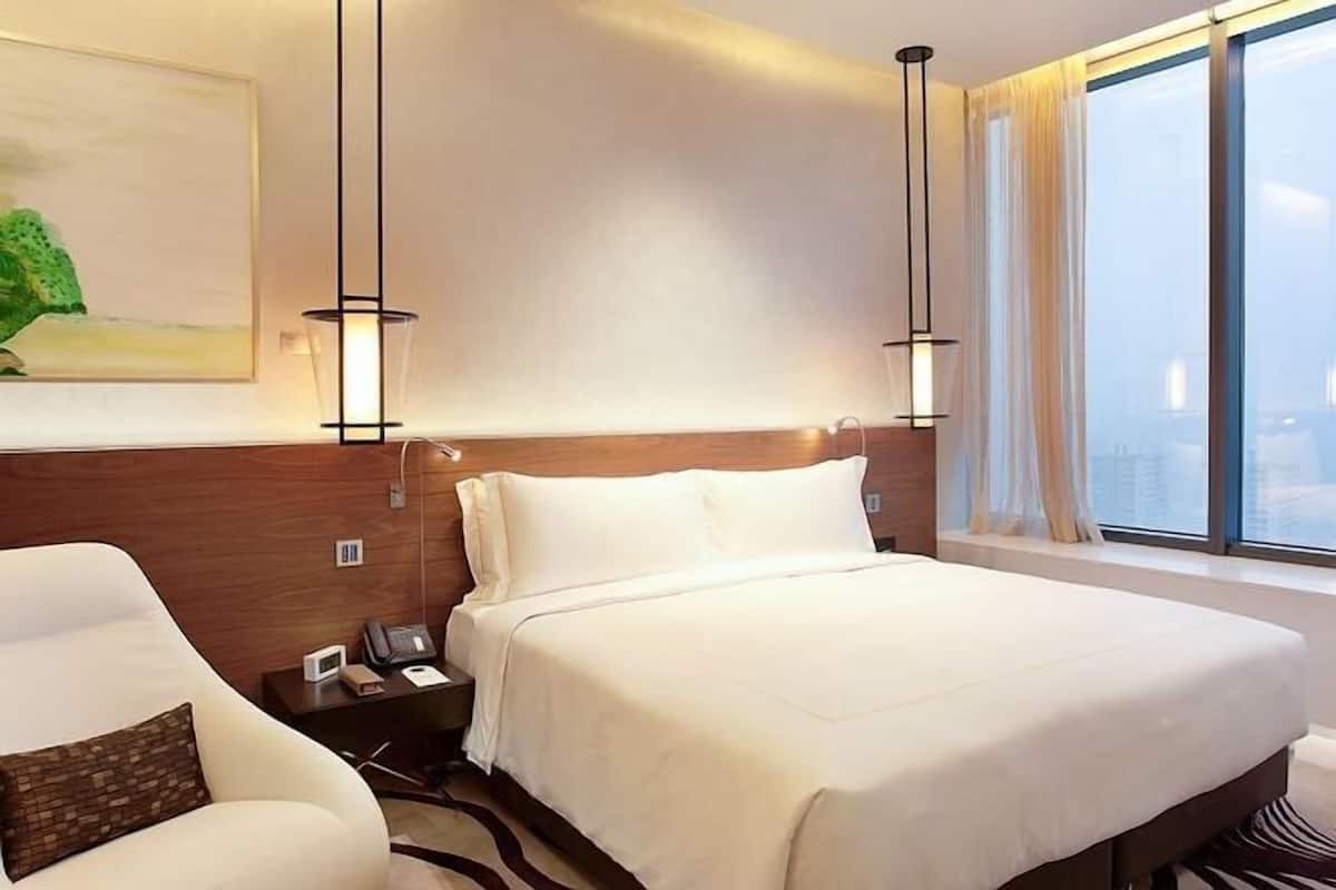 Une chambre d’hôtel avec un grand lit, une table de chevet avec une lampe, une chaise et une fenêtre avec des rideaux.