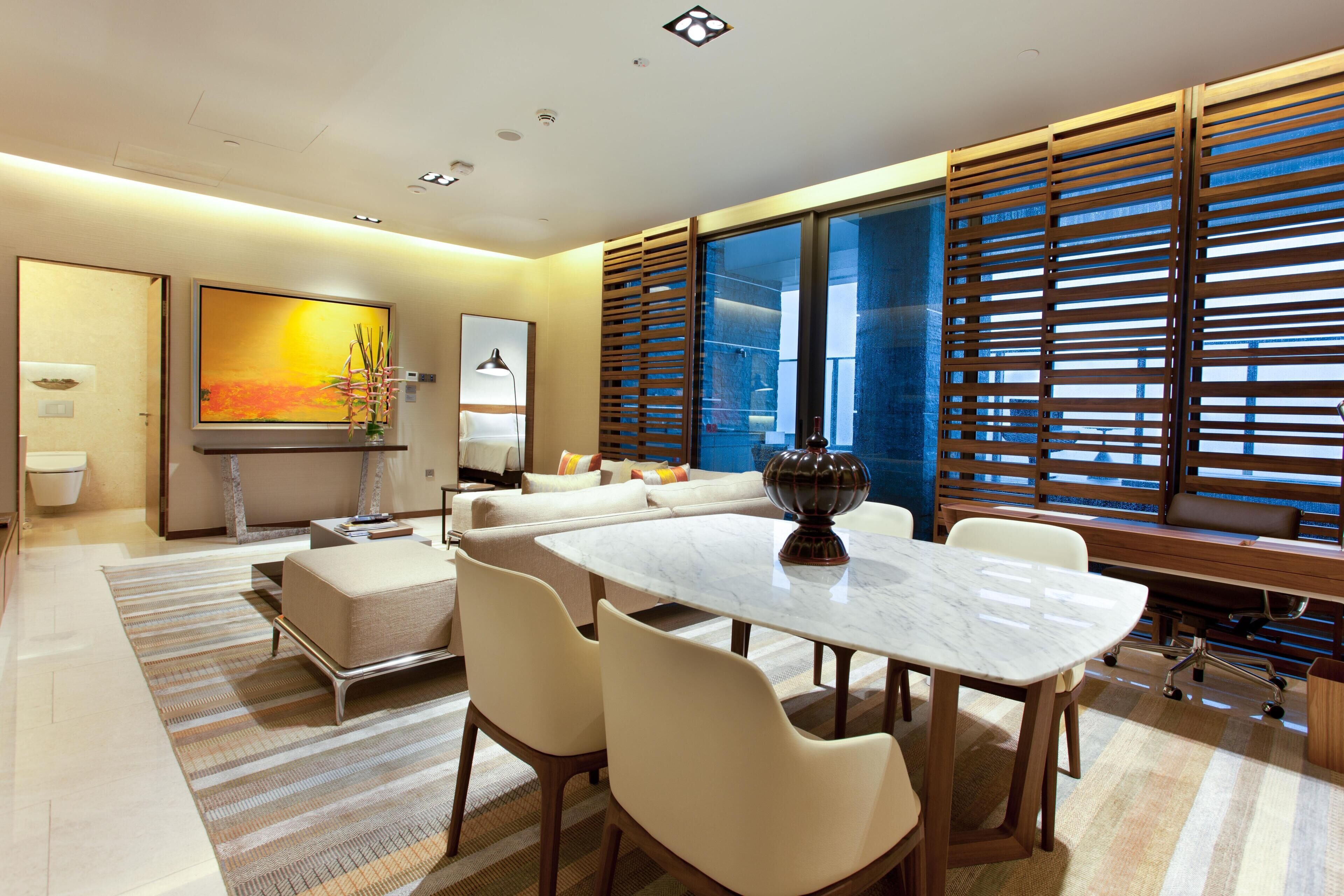 Una sala de estar moderna con una mesa de comedor, sofá y ventanas grandes con persianas.