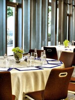 A dining area with tables set for two, clear glassware, and a decorative plant centerpiece.
