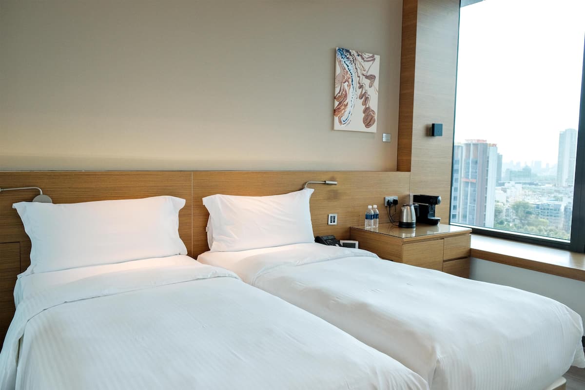 Une chambre d’hôtel avec un grand lit, une table de chevet avec une machine à café, un téléphone et une fenêtre donnant sur la ville.