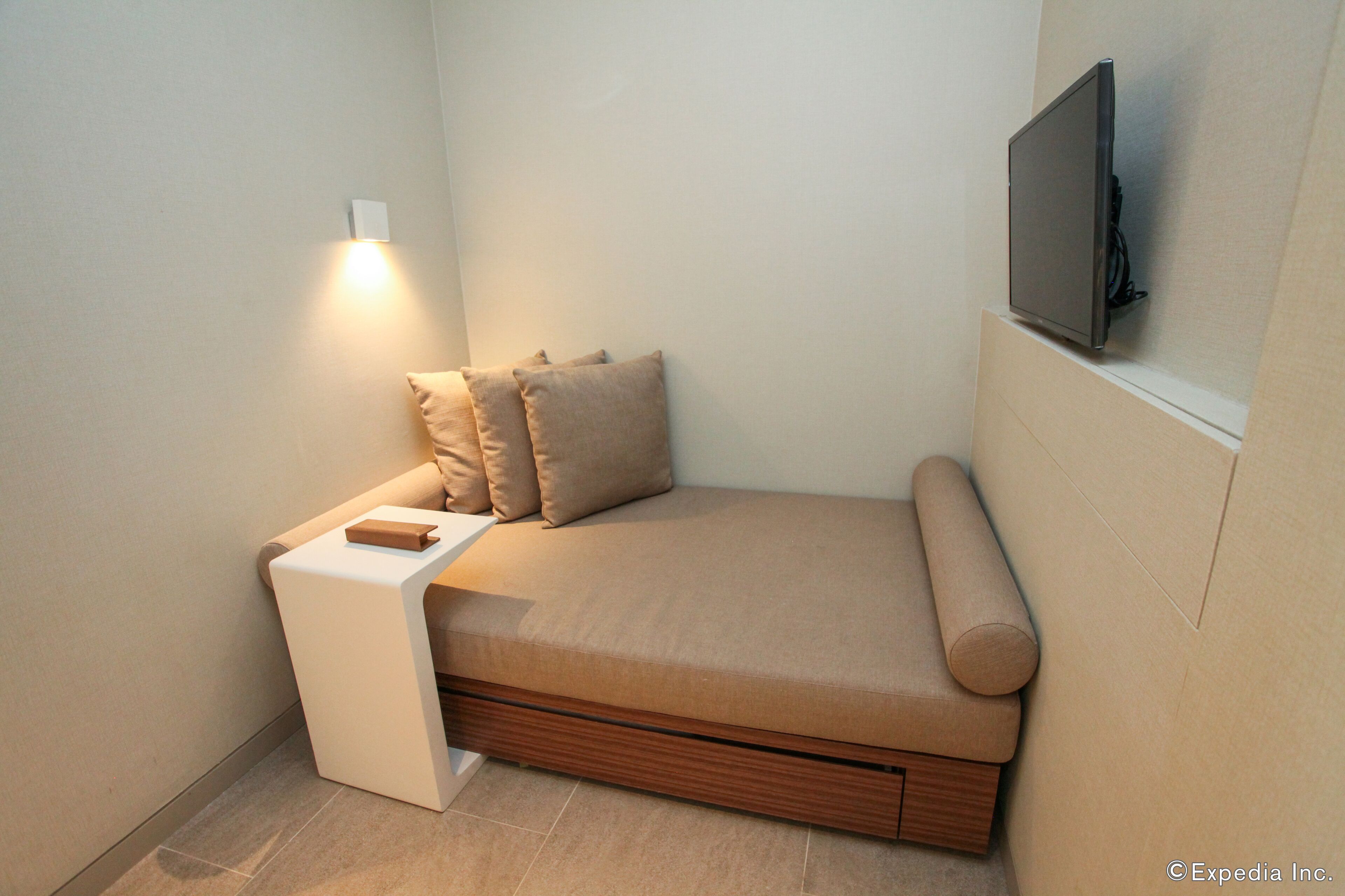 Ein kompakter, moderner Raum mit einem integrierten Bett, einem kleinen Nachttisch und einem an der Wand montierten Fernseher.