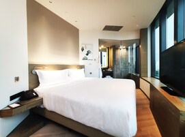 A modern hotel room with a large bed, a bedside table with a phone, a mirror, and a TV.