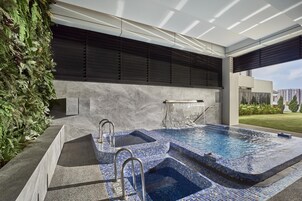 A modern indoor pool with a tiled design, a built-in hot tub, and a large window overlooking a cityscape.
