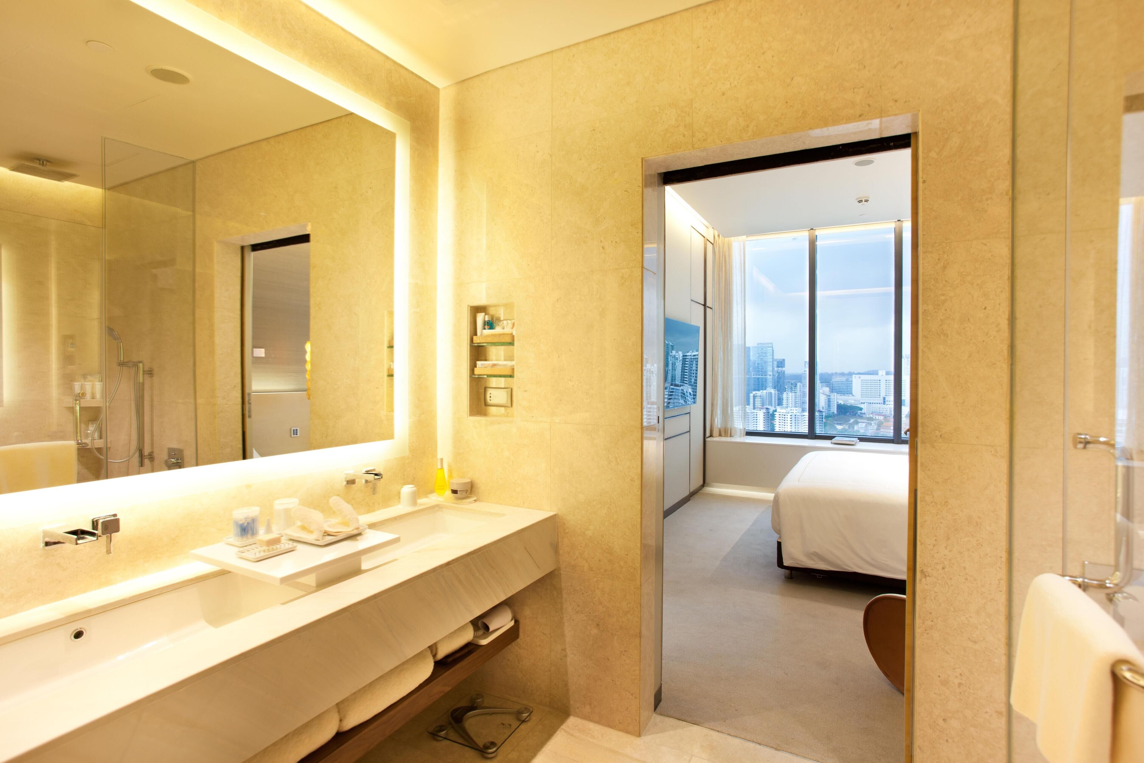 A modern hotel bathroom with a large mirror, dual sinks, and a shower.