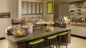A modern kitchen with a breakfast bar, including a coffee machine, fruit bowl, and bread baskets.