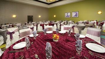 A banquet hall with round tables set for dining, featuring white tablecloths and purple sashes.