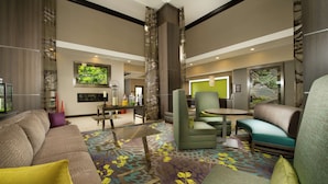 A modern hotel lobby with a large sofa, a dining table, and a green armchair.