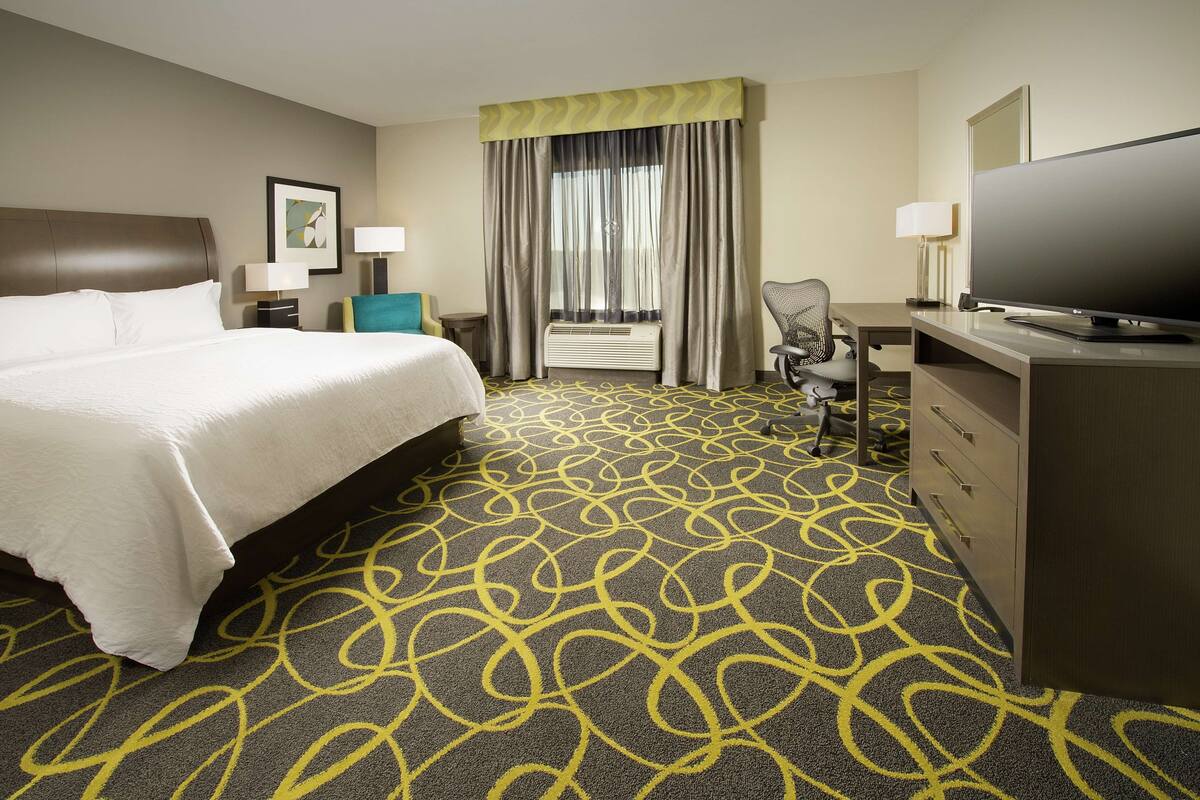 A hotel room with a large bed, a desk, a television, and a chair.