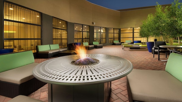 An outdoor seating area with a fire feature, cushioned seating, and large windows.