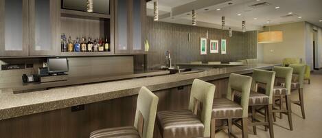 A bar area with a long counter, multiple stools, and a television mounted above.