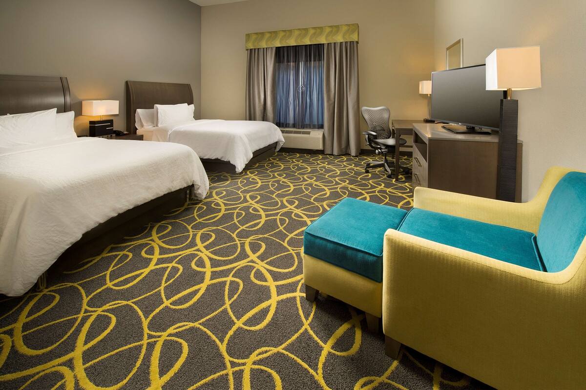 A hotel room with two beds, a desk, a television, and a sofa.