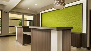 A reception area with a modern design, featuring a reception desk, a green textured wall, and a ceiling with recessed lighting.