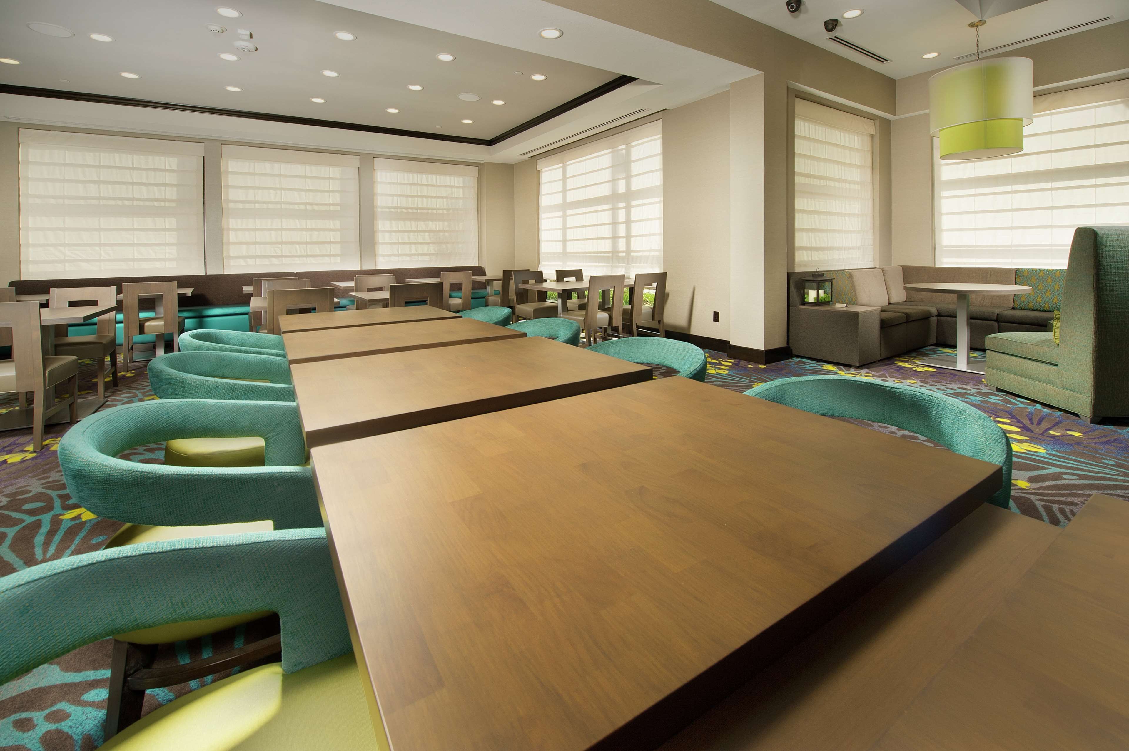 A conference room with long tables and teal chairs, large windows with blinds, and a patterned carpet.