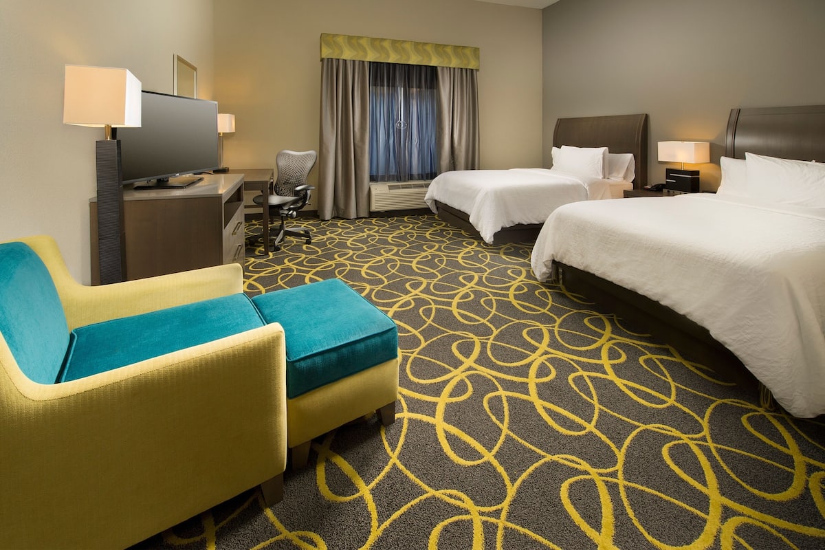 A hotel room with two beds, a desk with a TV, a chair, and a patterned carpet.