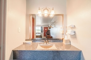 A bathroom with a granite countertop, a sink, and a mirror. There is a towel rack with towels and a soap dispenser on the wall. - Capital O Aurora Inn Monett US 60 (Aurora)