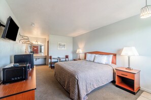 A hotel room with a bed, bedside table, lamp, TV, and a desk with a computer. - Capital O Aurora Inn Monett US 60 (Aurora)