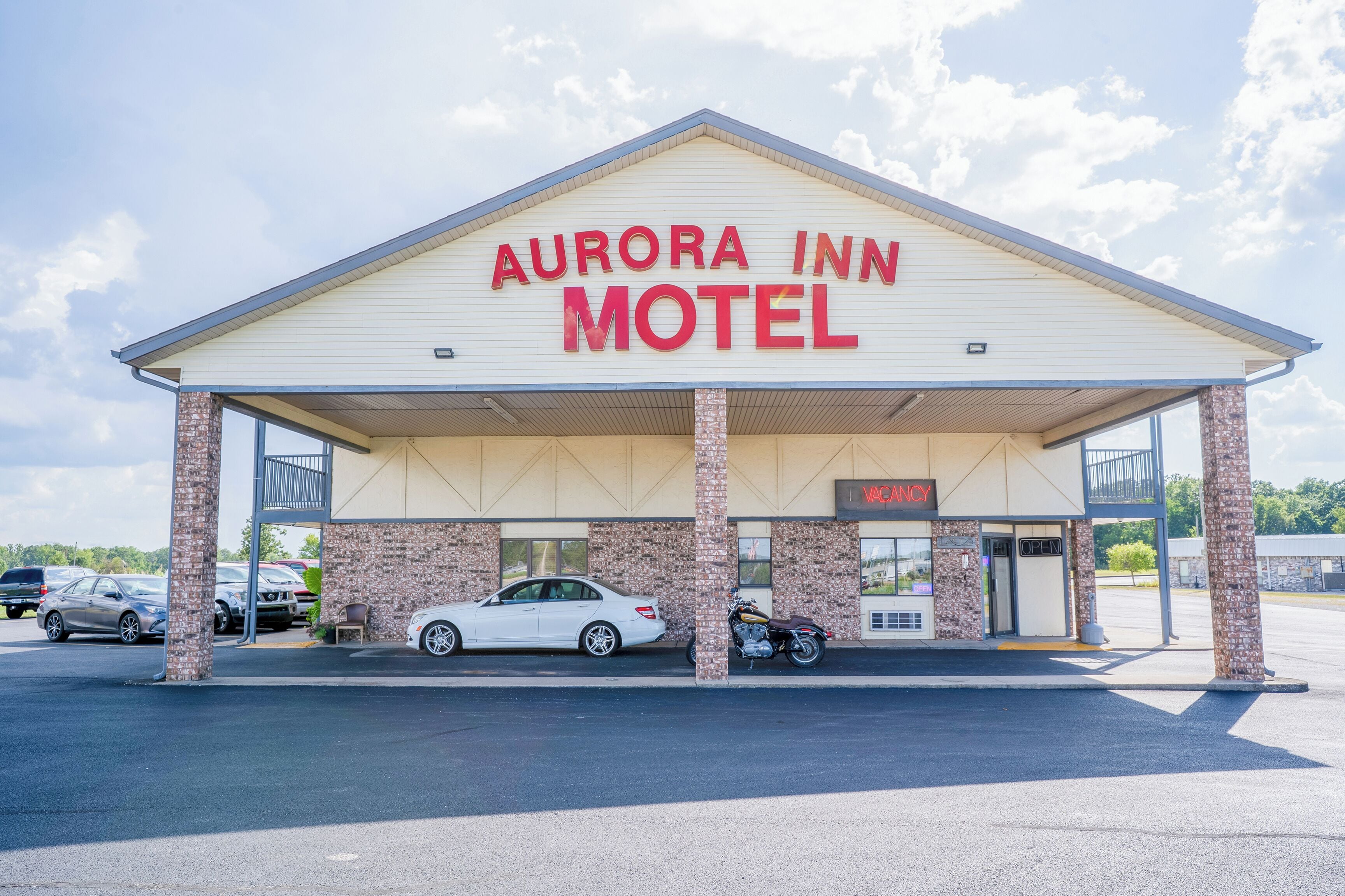 The exterior of the Aurora Inn Motel with a covered parking area, a brick facade, and a sign indicating a vacancy.
