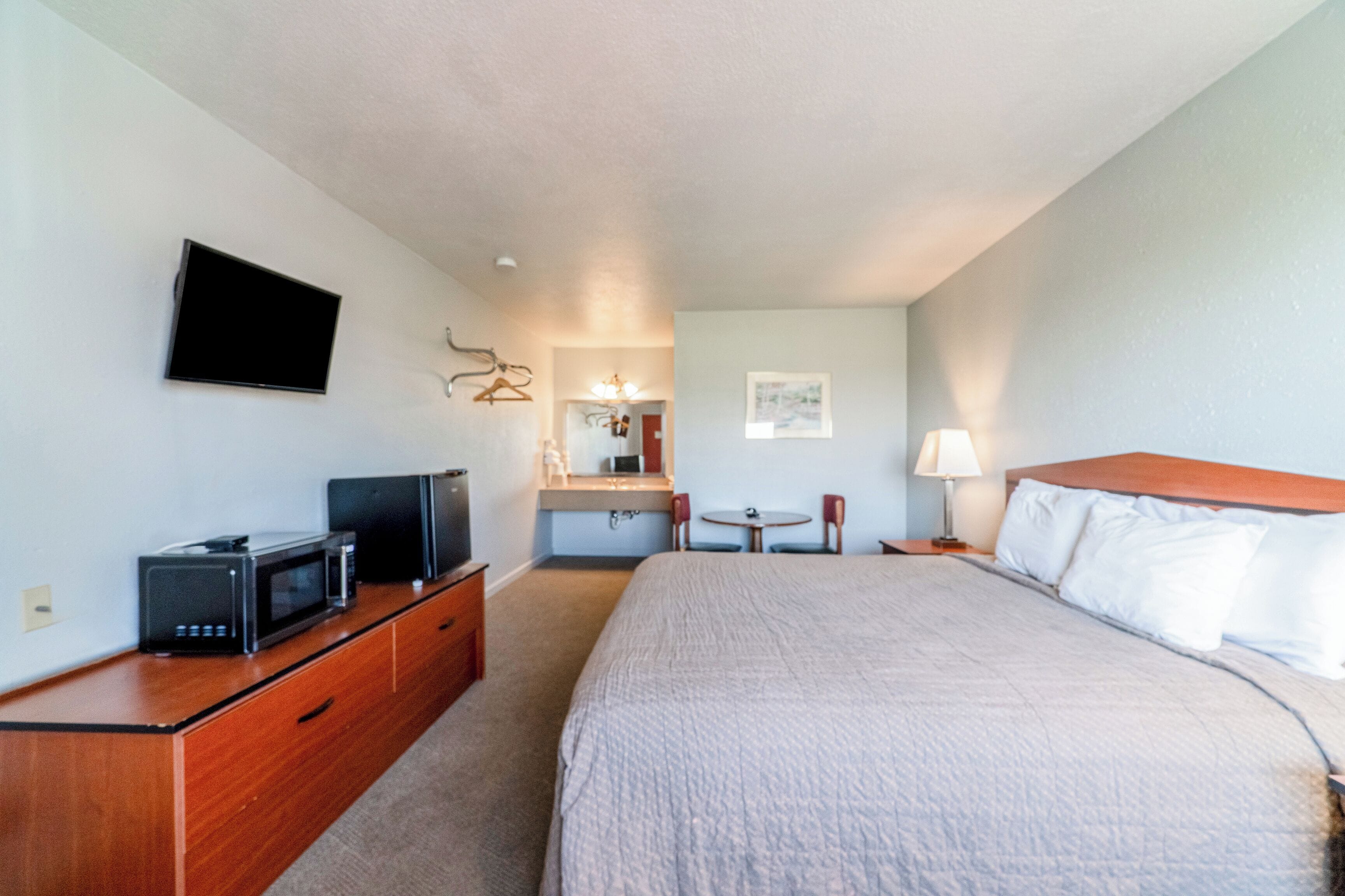 A hotel room with a bed, a TV, a desk with a computer, a chair, a lamp, and a small table.