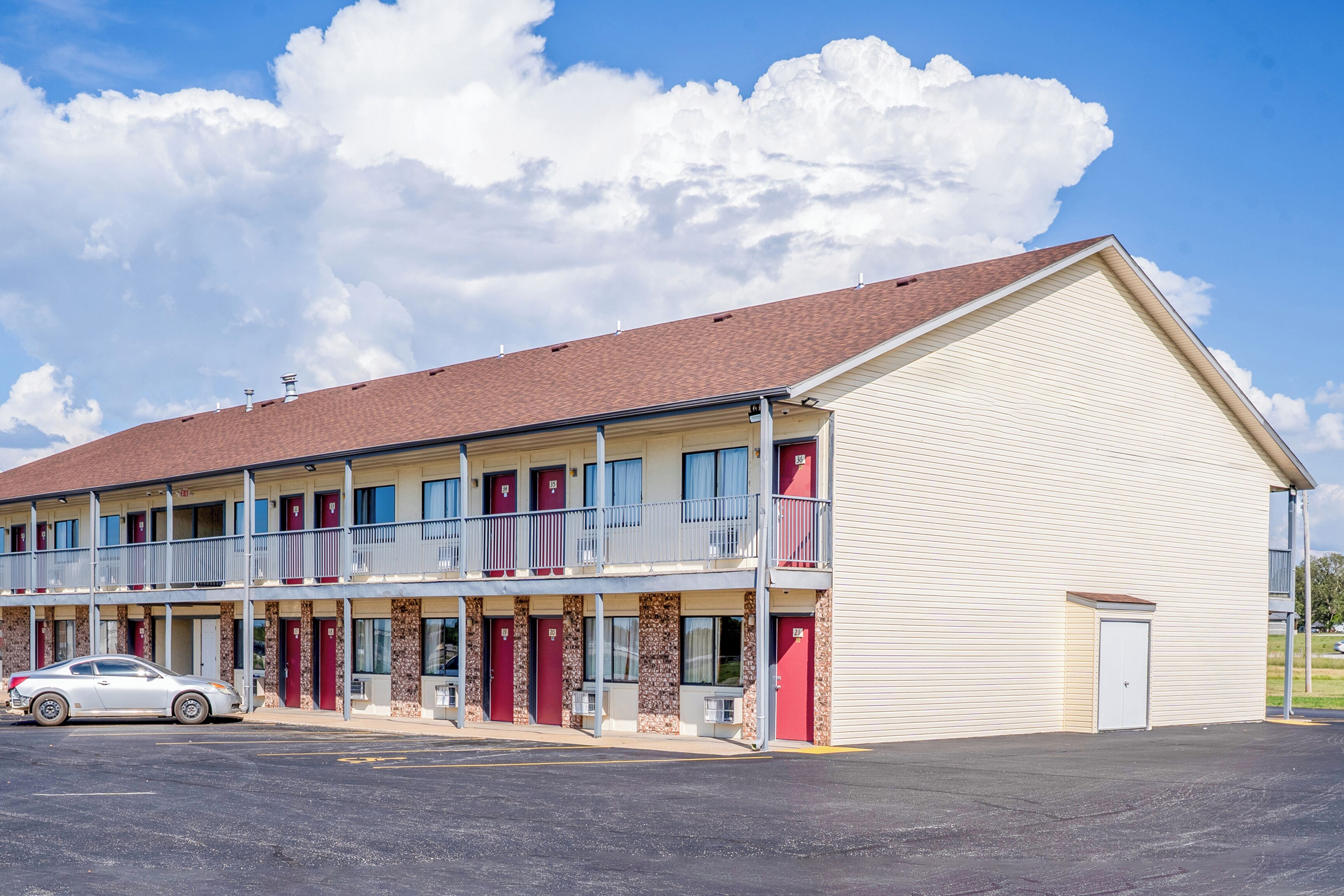 A motel with a two-story structure, multiple rooms with red doors, and a parking lot.