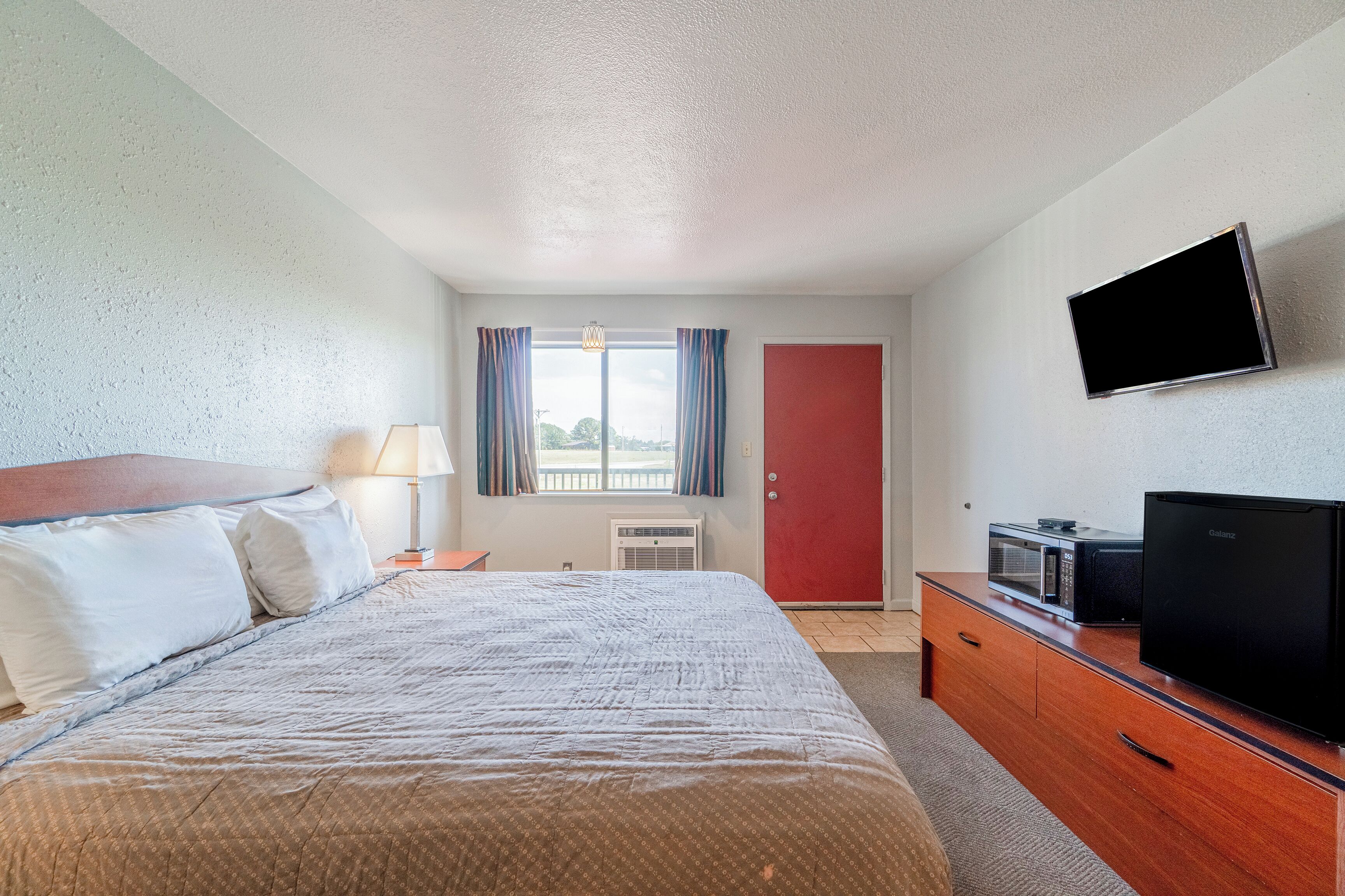 Quarto de hotel com cama, televisão, micro-ondas e porta vermelha.