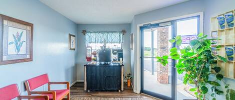 A reception area with a desk, chairs, a potted plant, and a view through a glass door.