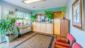 A room with a wooden cabinet, a red chair, and a large window with curtains. - Capital O Aurora Inn Monett US 60 (Aurora)