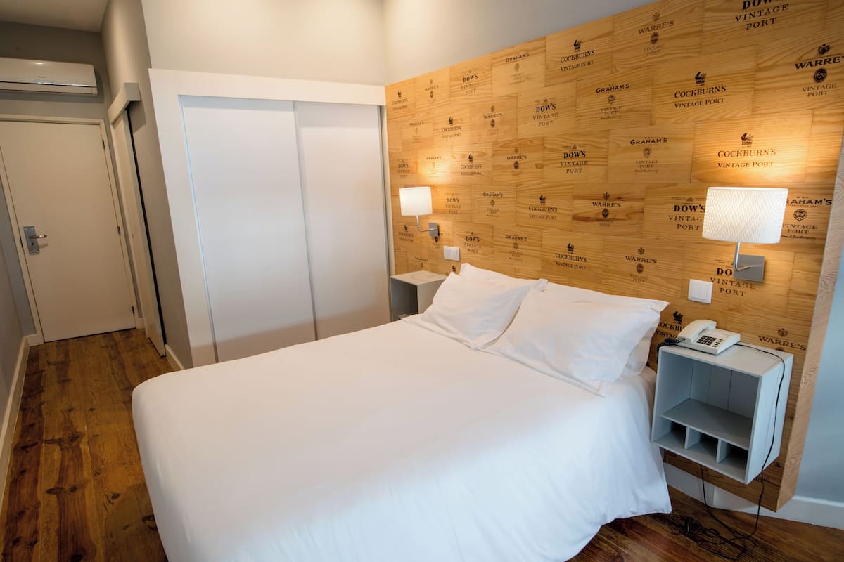 A hotel room with a wooden headboard, a bed with white linens, a bedside table with a lamp, and a phone.