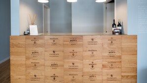 Een receptiebalie met drie hanglampen, een vaas met rietstengels en twee flessen wijn. De balie heeft een houten paneeldecoratie met diverse havenaam.'