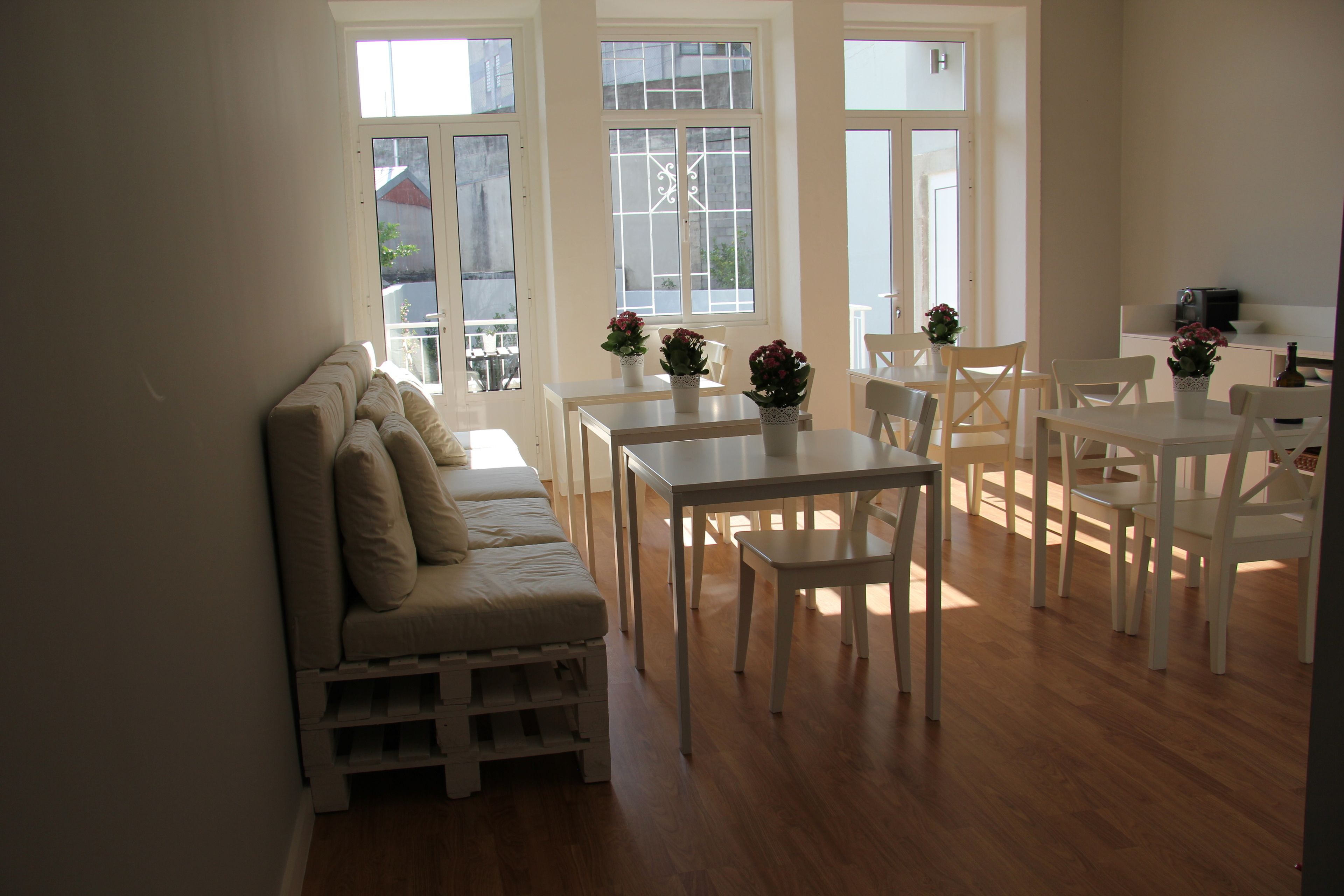 A dining area with white furniture, including a table and chairs, and a sofa with cushions. There are potted plants on the table.