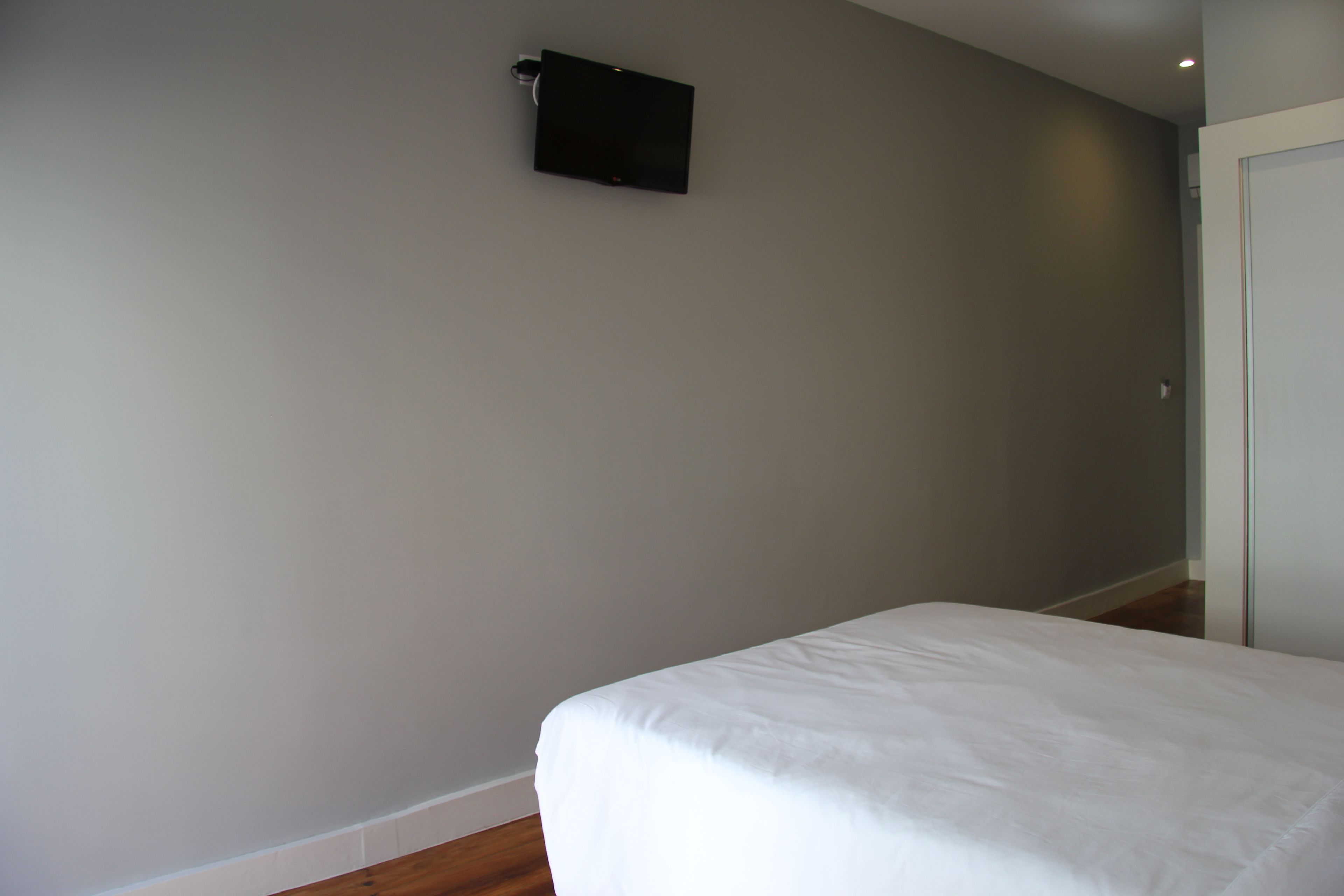 Quarto com cama, televisão de tela plana na parede e uma porta.