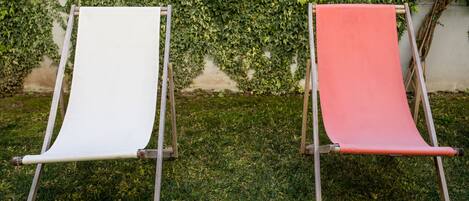 Two canvas chairs with metal frames, positioned on a grassy lawn with a wall covered in ivy behind them.