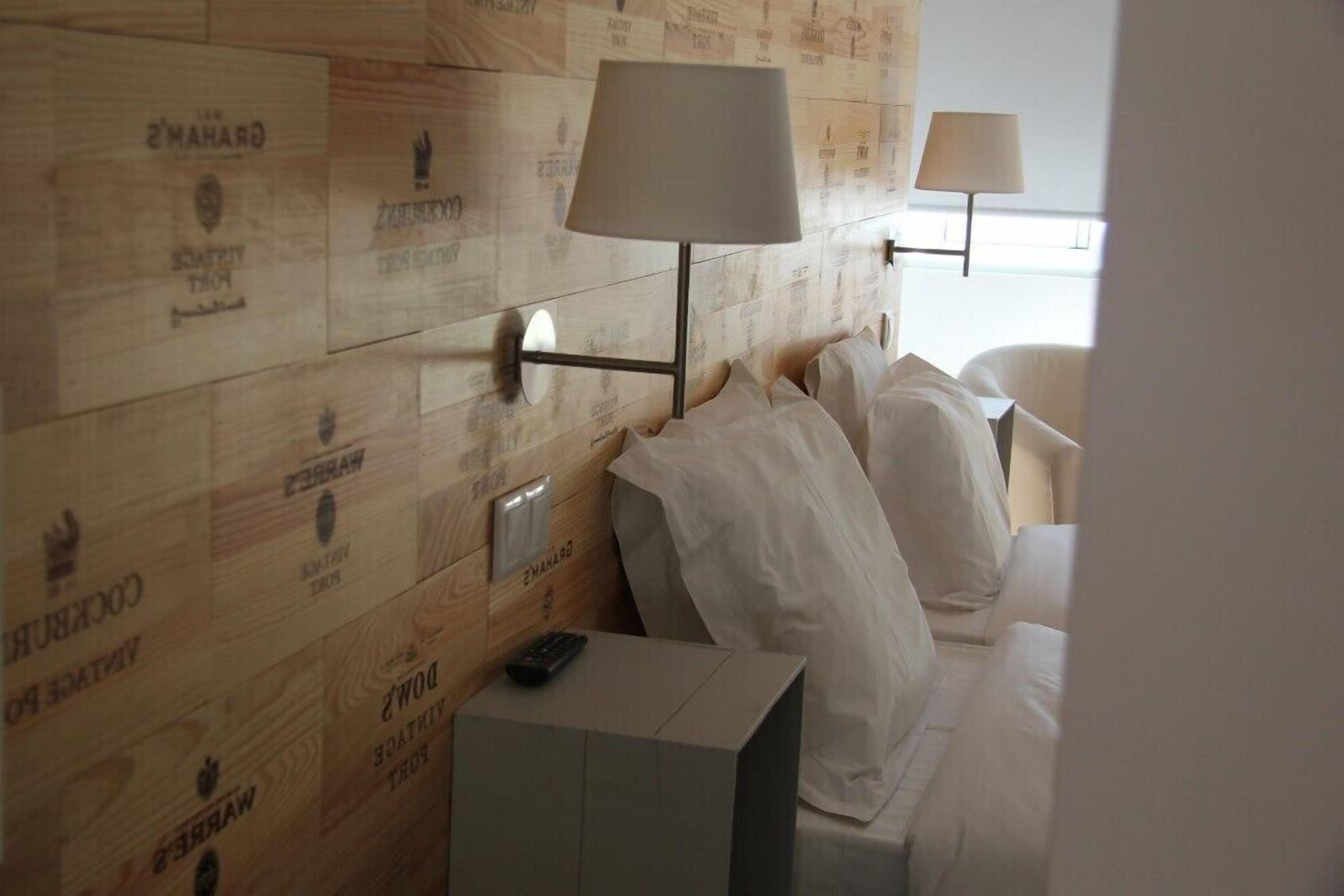 Een hotelkamer met een houten hoofdeinde, twee bedlampen, een bed met witte lakens en een klein nachtkastje met een afstandsbediening.