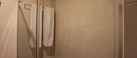 A glass-enclosed shower with beige tiles and a white towel hanging on the door.