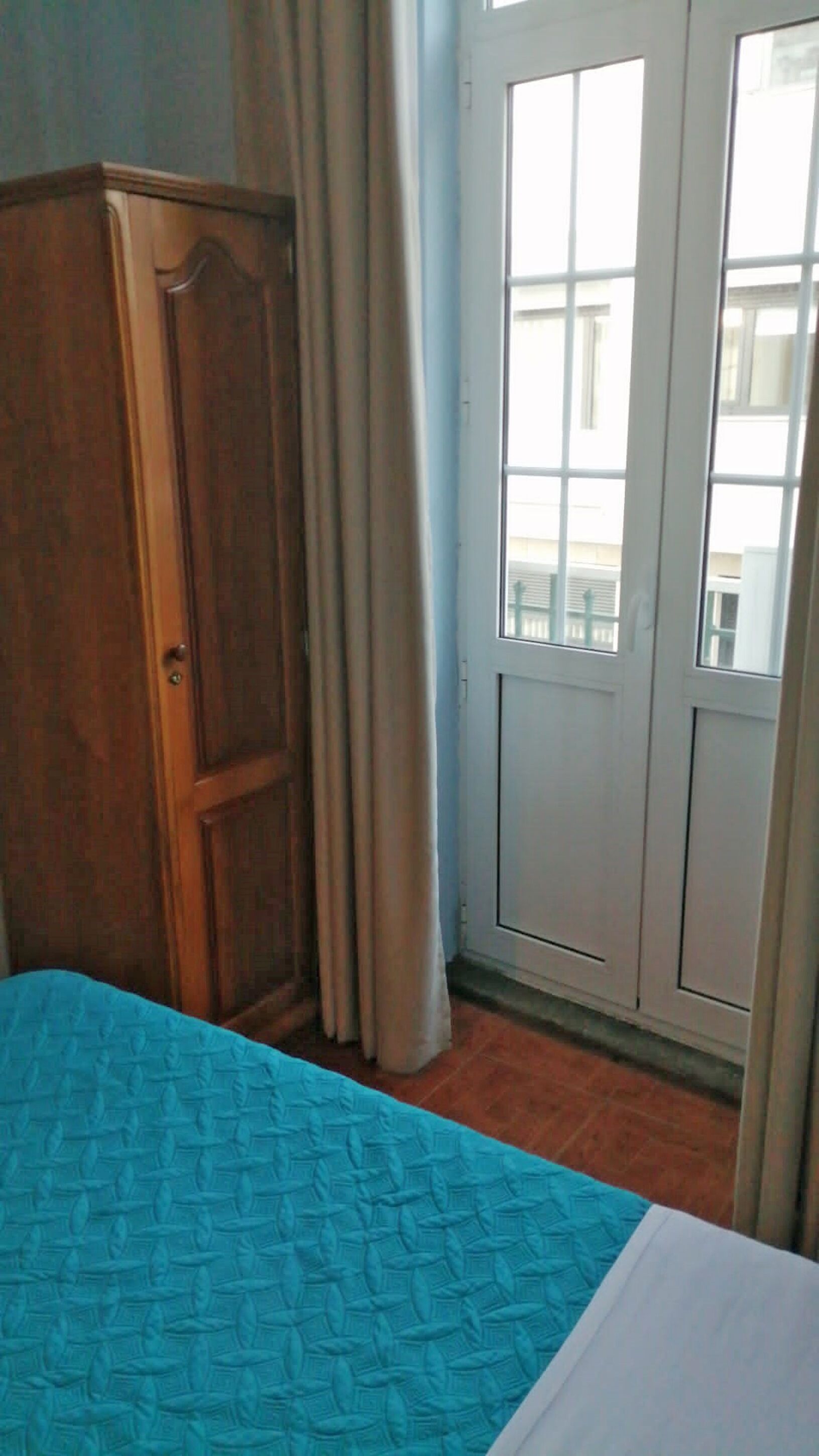 Una habitación con cama, un armario de madera, una puerta con ventanal y cortinas.