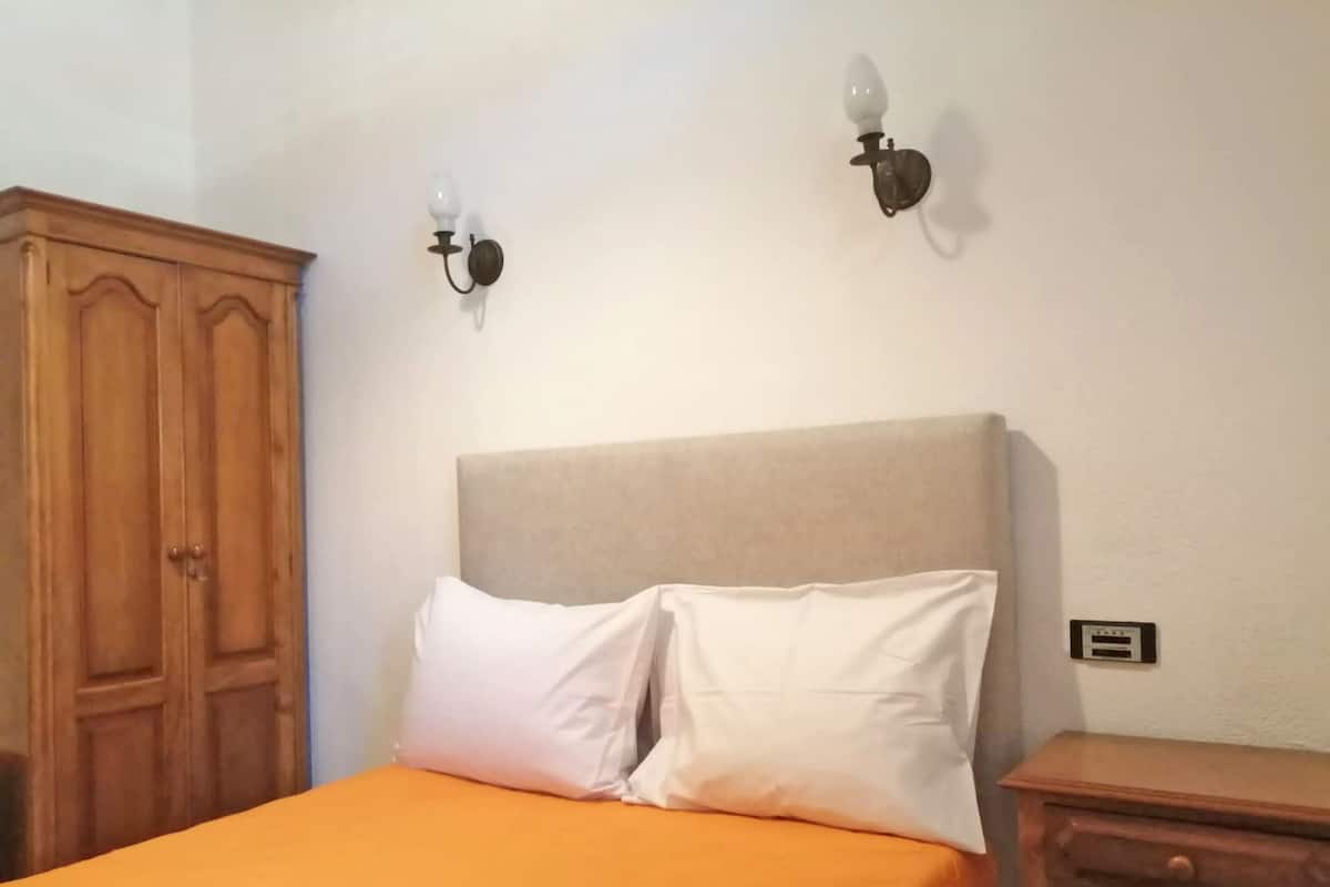 A bedroom with a bed, two wall-mounted light fixtures, a wooden wardrobe, and a small bedside table.