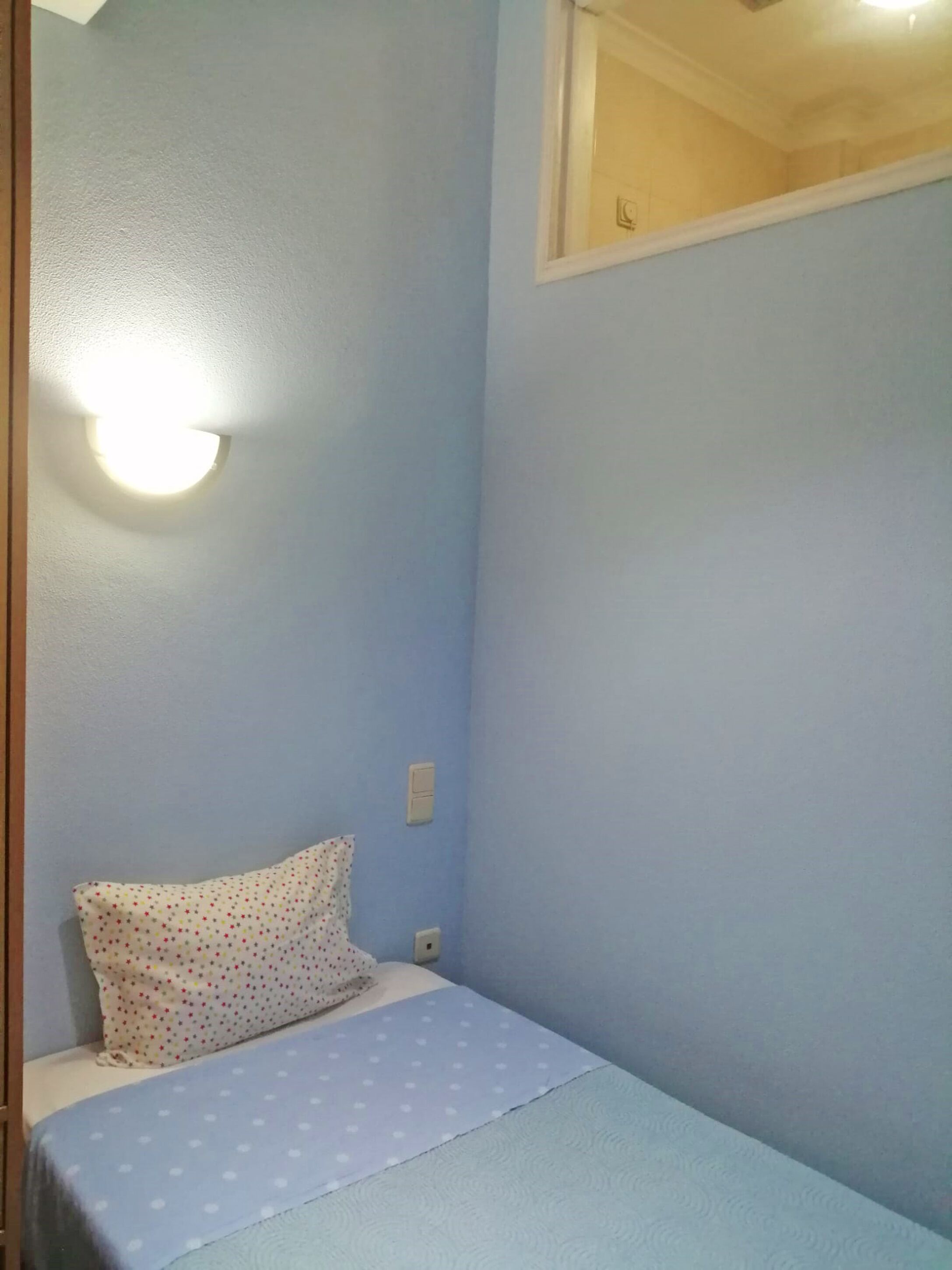 Habitación pequeña con una cama individual, pared azul, almohada blanca y cubrecama azul.