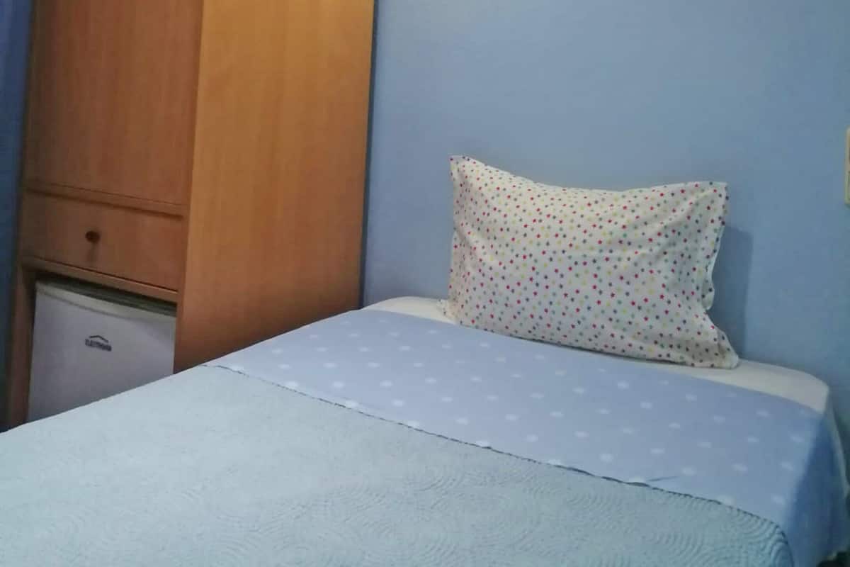 A bedroom with a wooden wardrobe, a bed with a white pillow, and a wall-mounted light.