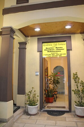 A hotel entrance with a sign indicating "Residencia Vale Formoso" and contact information. There are potted plants at the entrance. - Residencial Vale Formoso (Porto)
