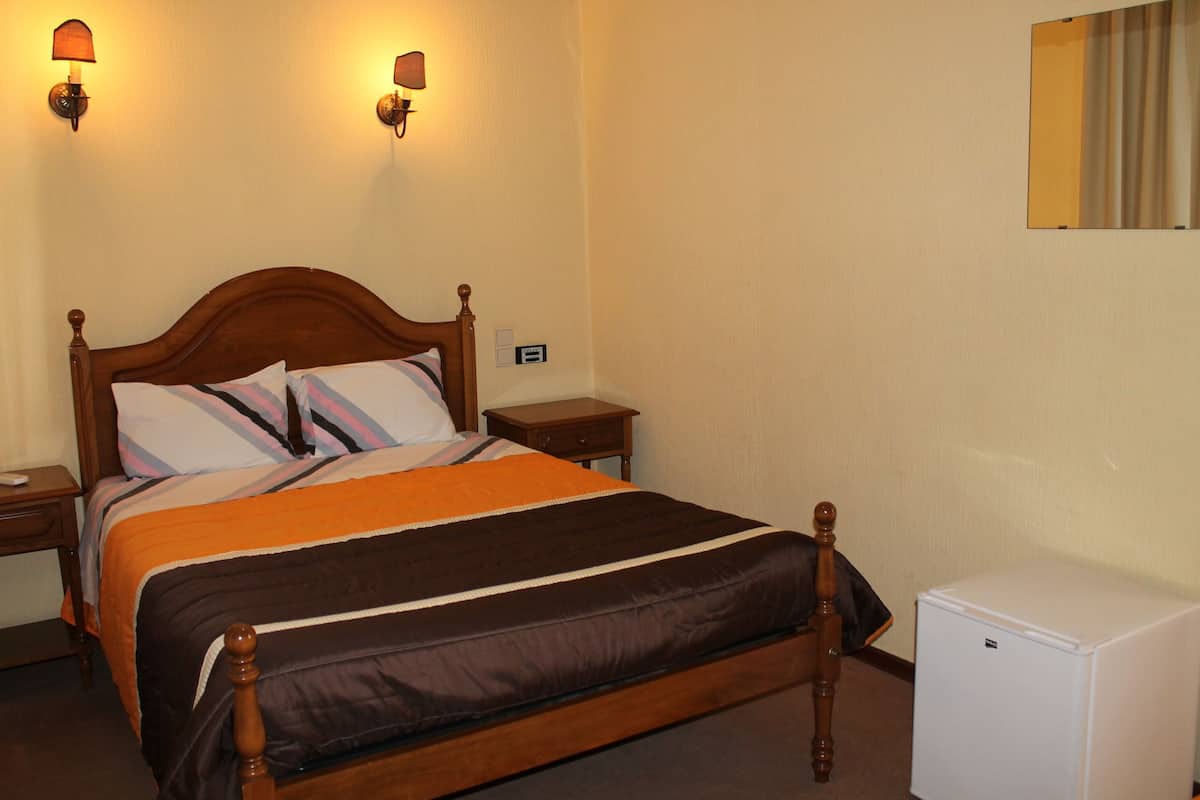 A neatly made bed with a wooden headboard, two bedside lamps, a small bedside table, and a white refrigerator.