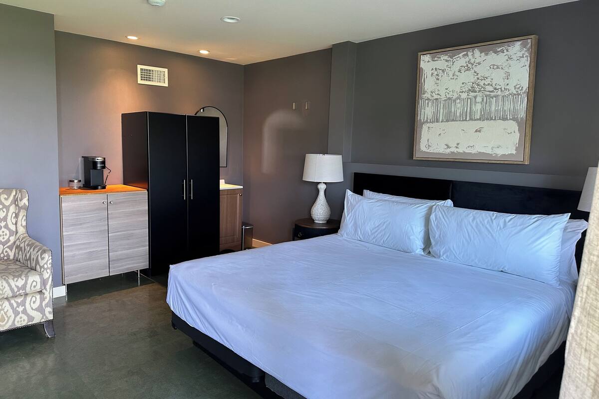Une chambre d’hôtel avec un grand lit, une armoire, un bureau avec une machine à café, une lampe et un tableau au mur.