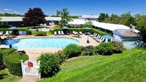 A swimming pool surrounded by lounge chairs and umbrellas, with a white picket fence and well-maintained lawn.